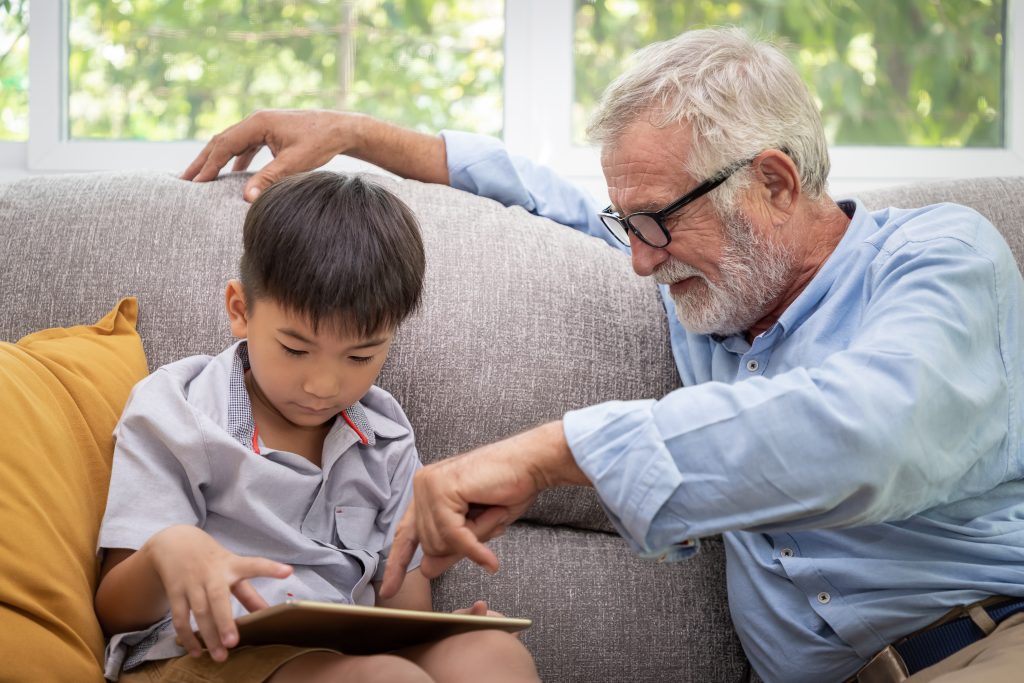 Happy boy grandson playing game on tablet with old senior man gr